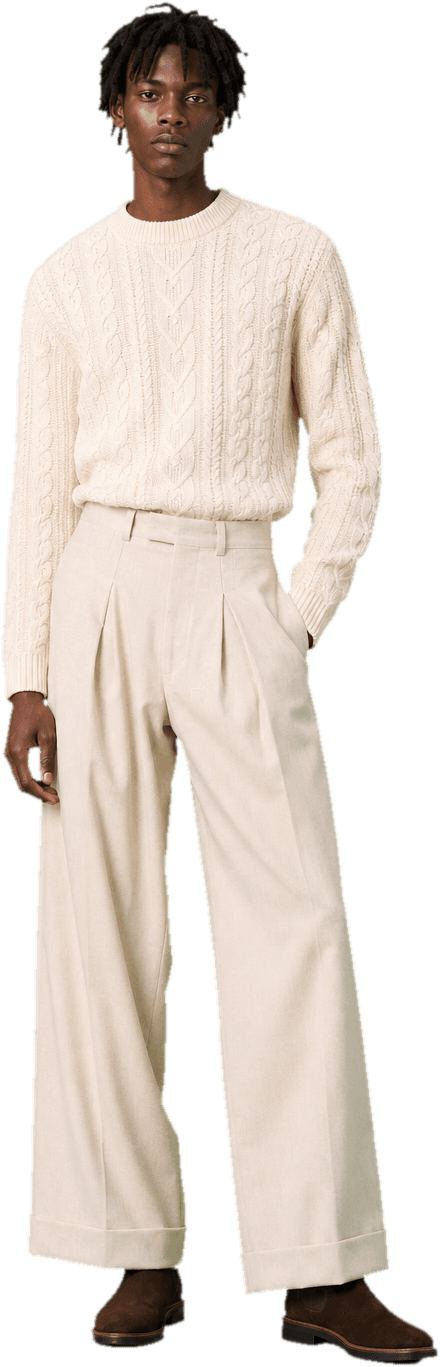 An ivory cable-knit fisherman's sweater tucked into wide-leg cream wool trousers, with brown suede chelsea boots